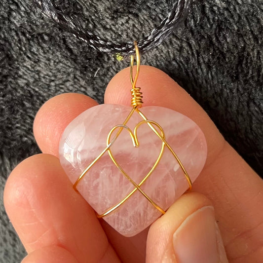 Wire-wrapped rose quartz heart necklace: a gold wire intricately wraps around a polished rose quartz heart pendant, hanging on a delicate chain.  The wire makes a heart shape in the middle of the rose quartz heart.