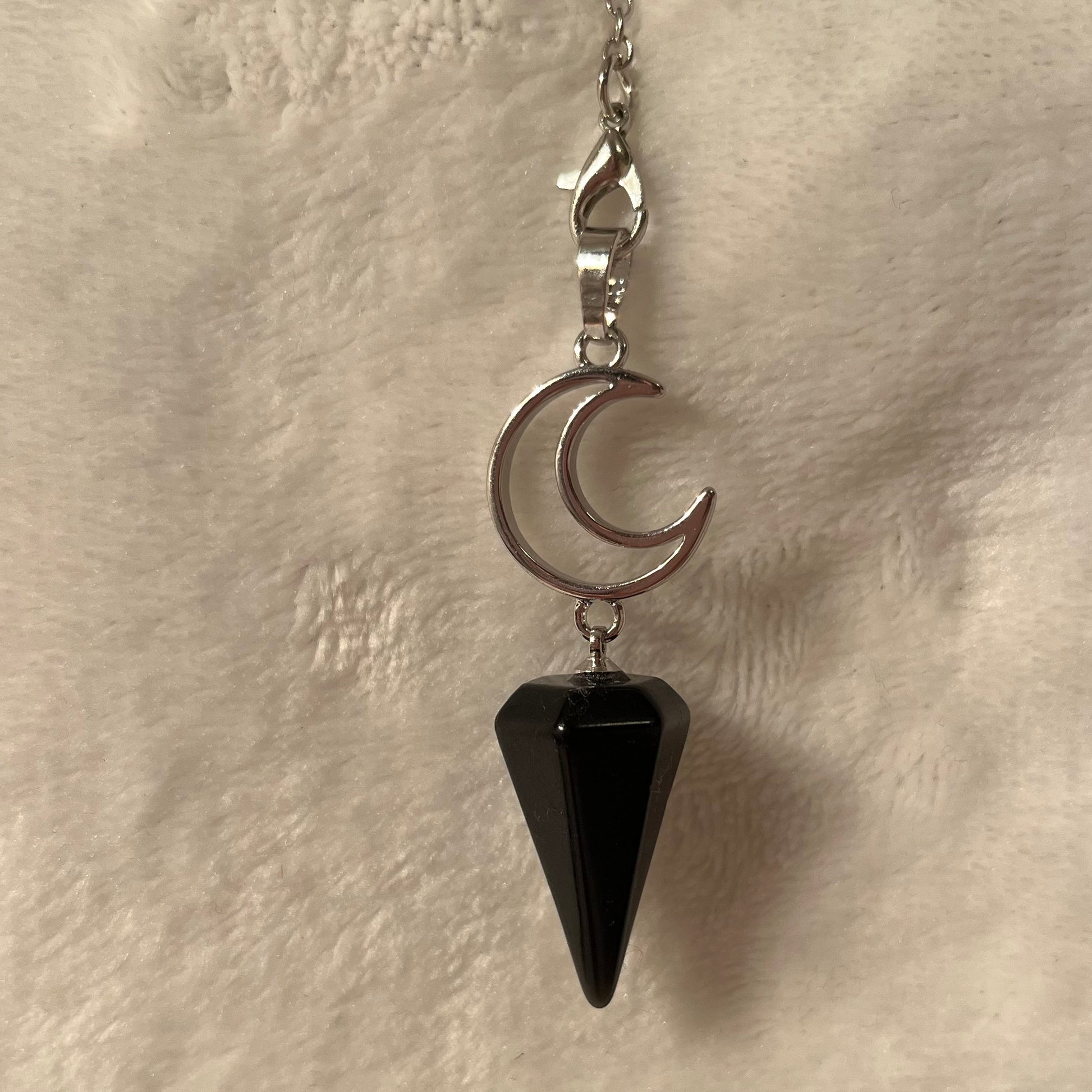 Close up of a 1 inch black obsidian pendulum attarched to a silver crescent moon, both connected to an 8 inch silver chain