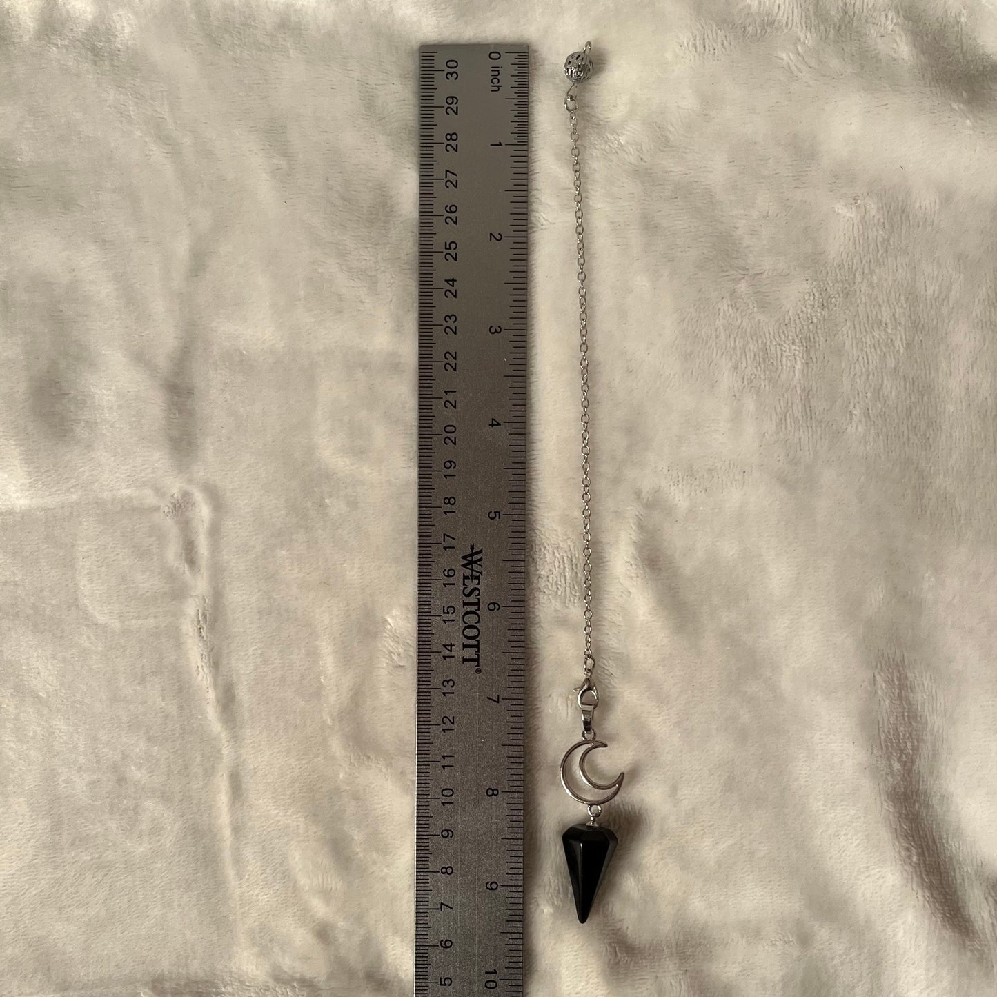 1 inch black obsidian pendulum attarched to a silver crescent moon, both connected to an 8 inch silver chain, next to a silver ruler against a white backround