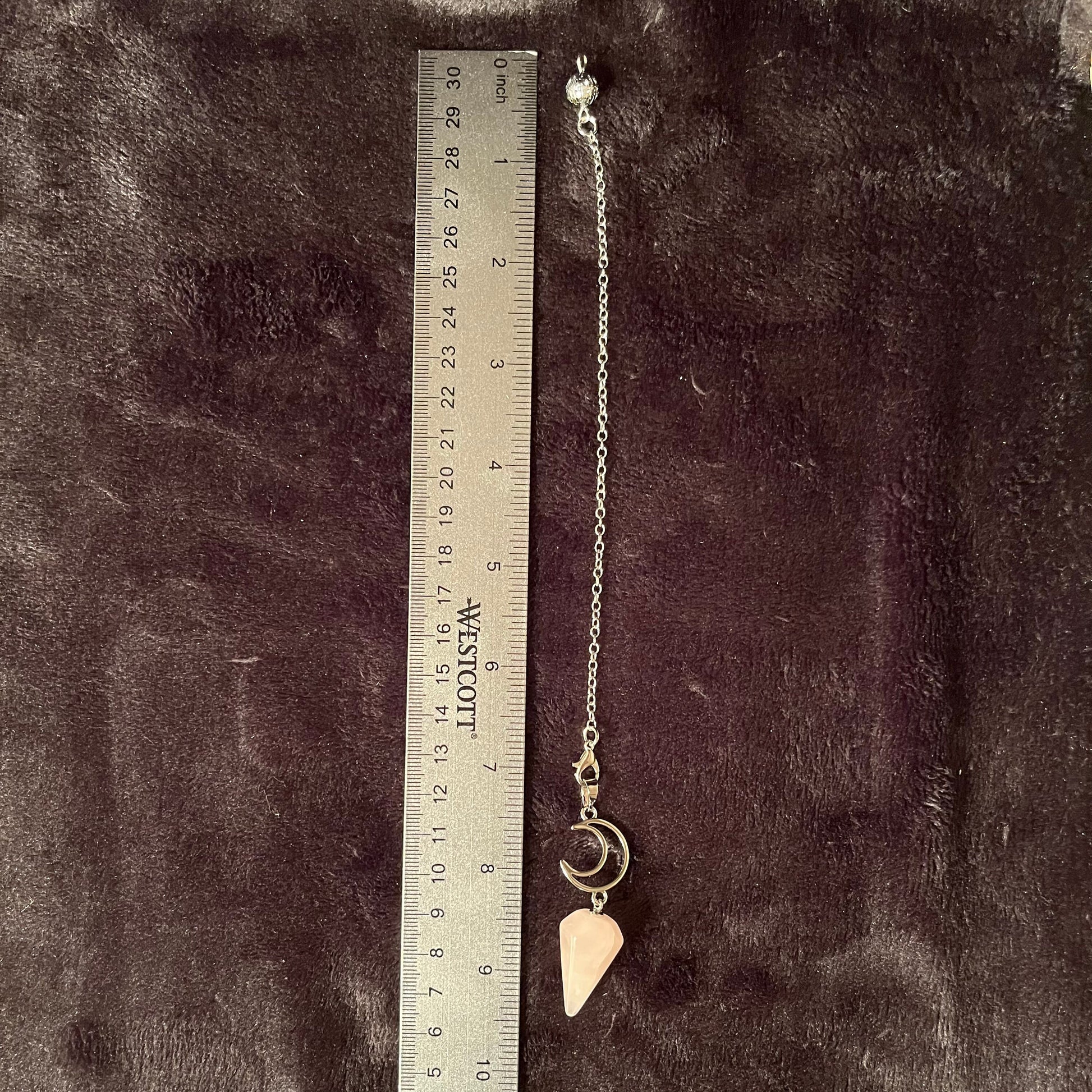 1 inch rose quartz pendulum attatched to an 8 inch silver chain including chakra beads amd a silver crescent moon displayed next to a silver ruler on a black background