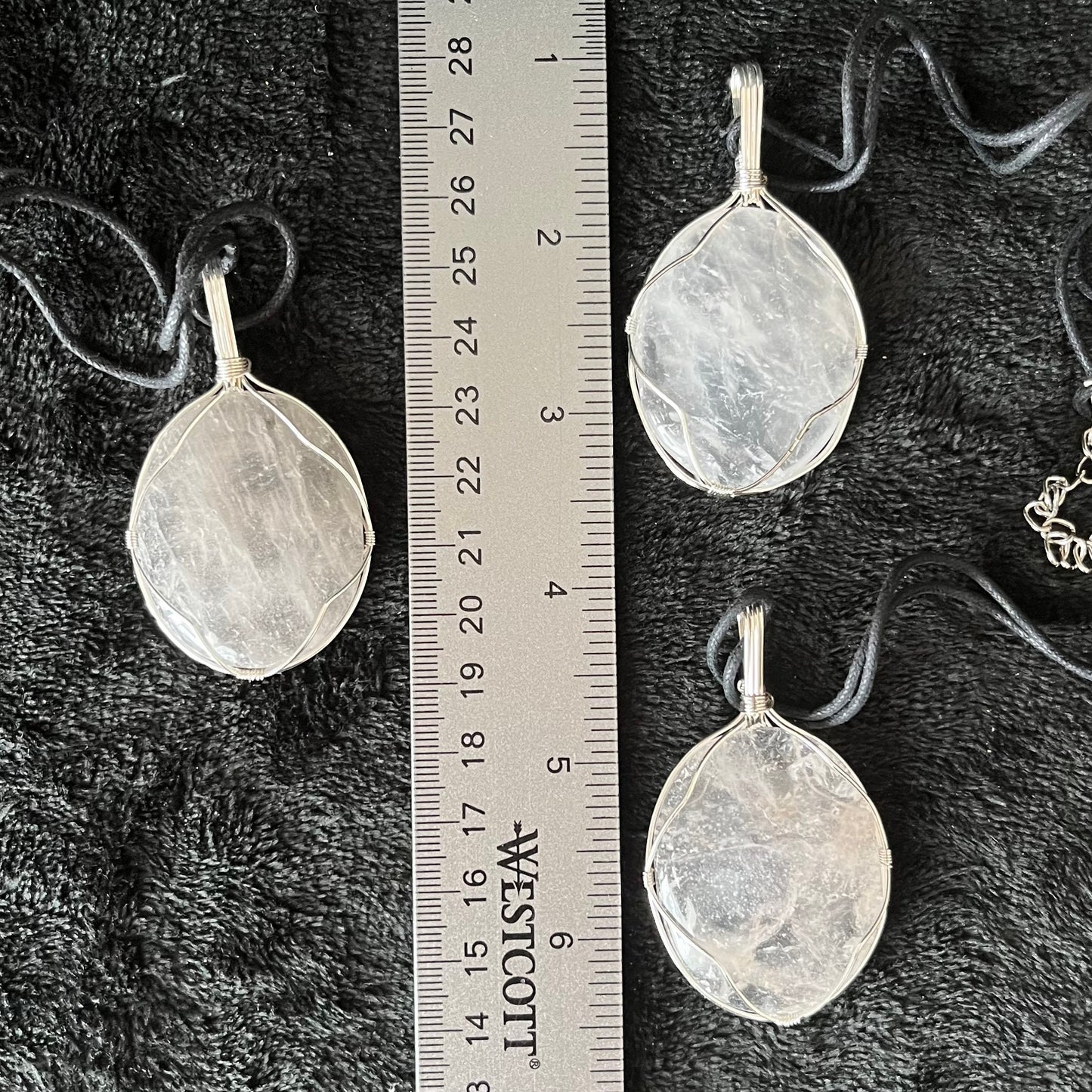 3 clear quartz worry stones beautifully silver wire wrapped in a way that frames the stone beautifully allowing access to the smoothe concave side on the back.  pe dants are approximately 2 inches long and attatched to adjustable black cords. displayed next to a ruler