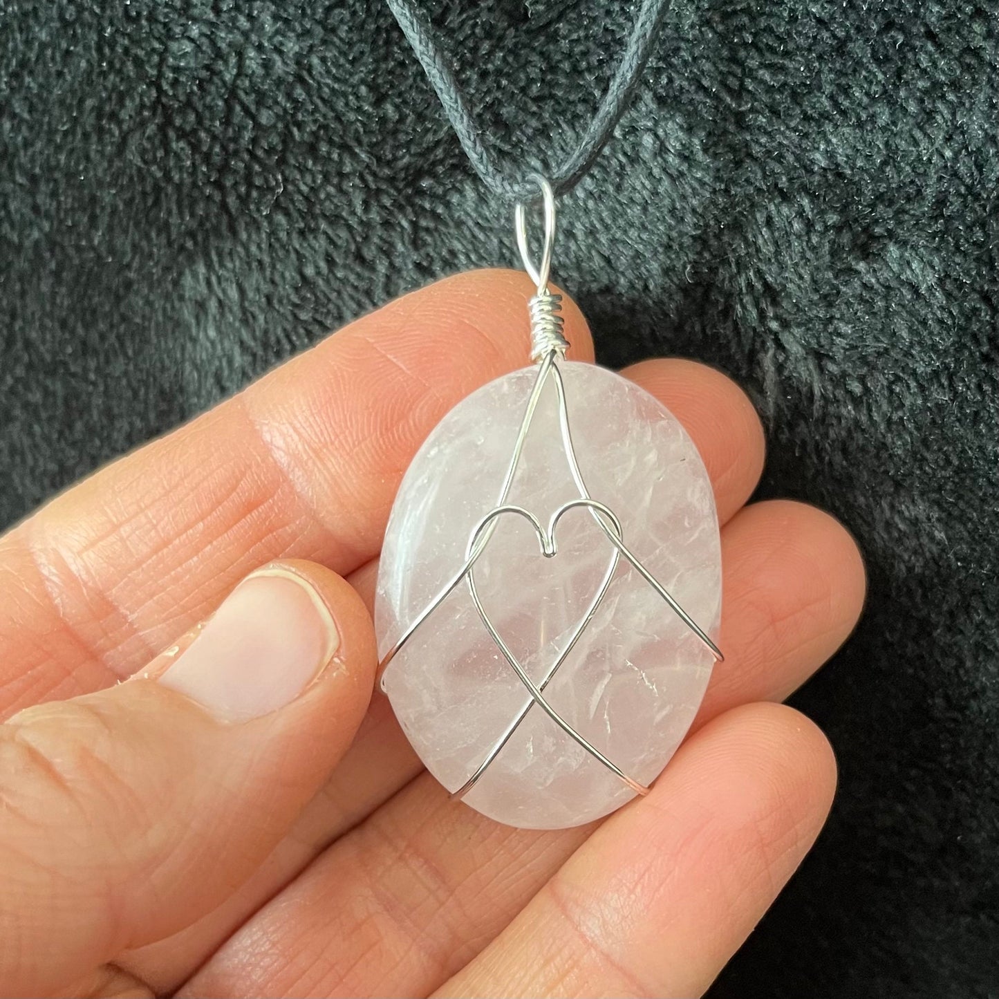 ornately silver wire wrapped translicent pink rose quartz worry stone pendant, approximately 1 1/4" long, attarched to an adjustable black cord.   The ailver wire male a heart shape in the center pf the rose quartz stone.
